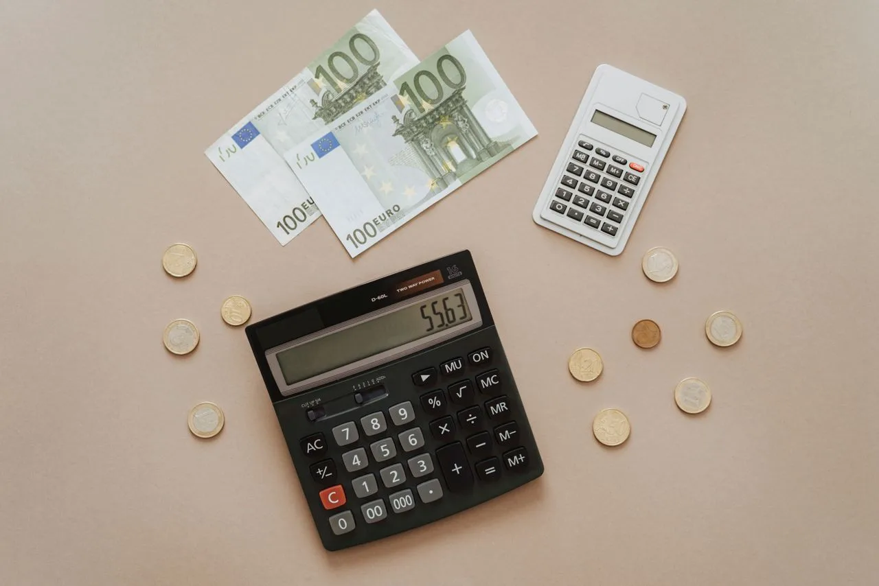 Billets et pièces en euros posés à plat près de deux calculatrices