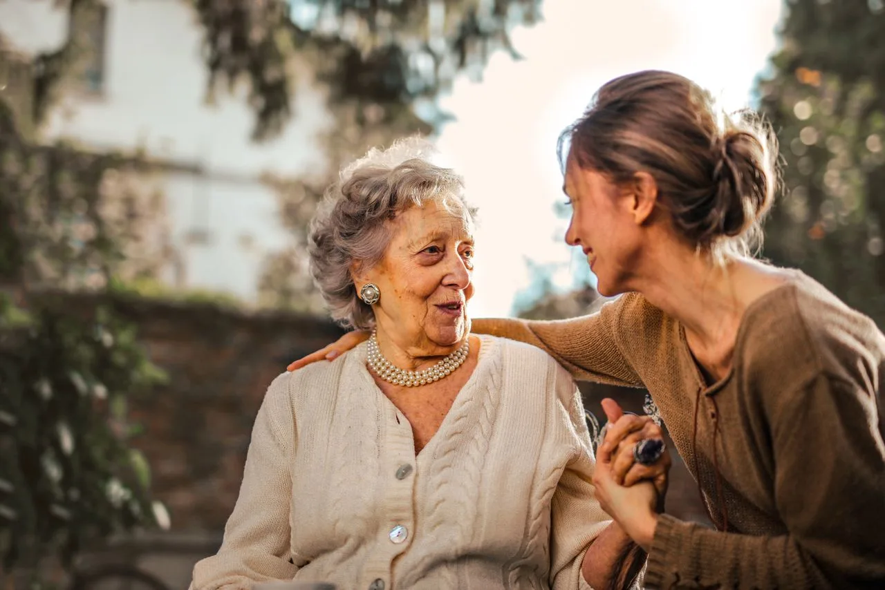 Une mère âgée et sa fille adulte se tiennent la main, dans un jardin